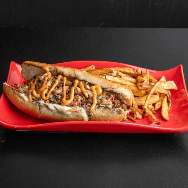 A soul-food cheesesteak sandwich with orange sauce and fries on a red plate.