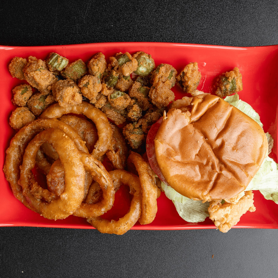 A fried chicken sandwich with lettuce, onion rings, and fried okra on a red plate.